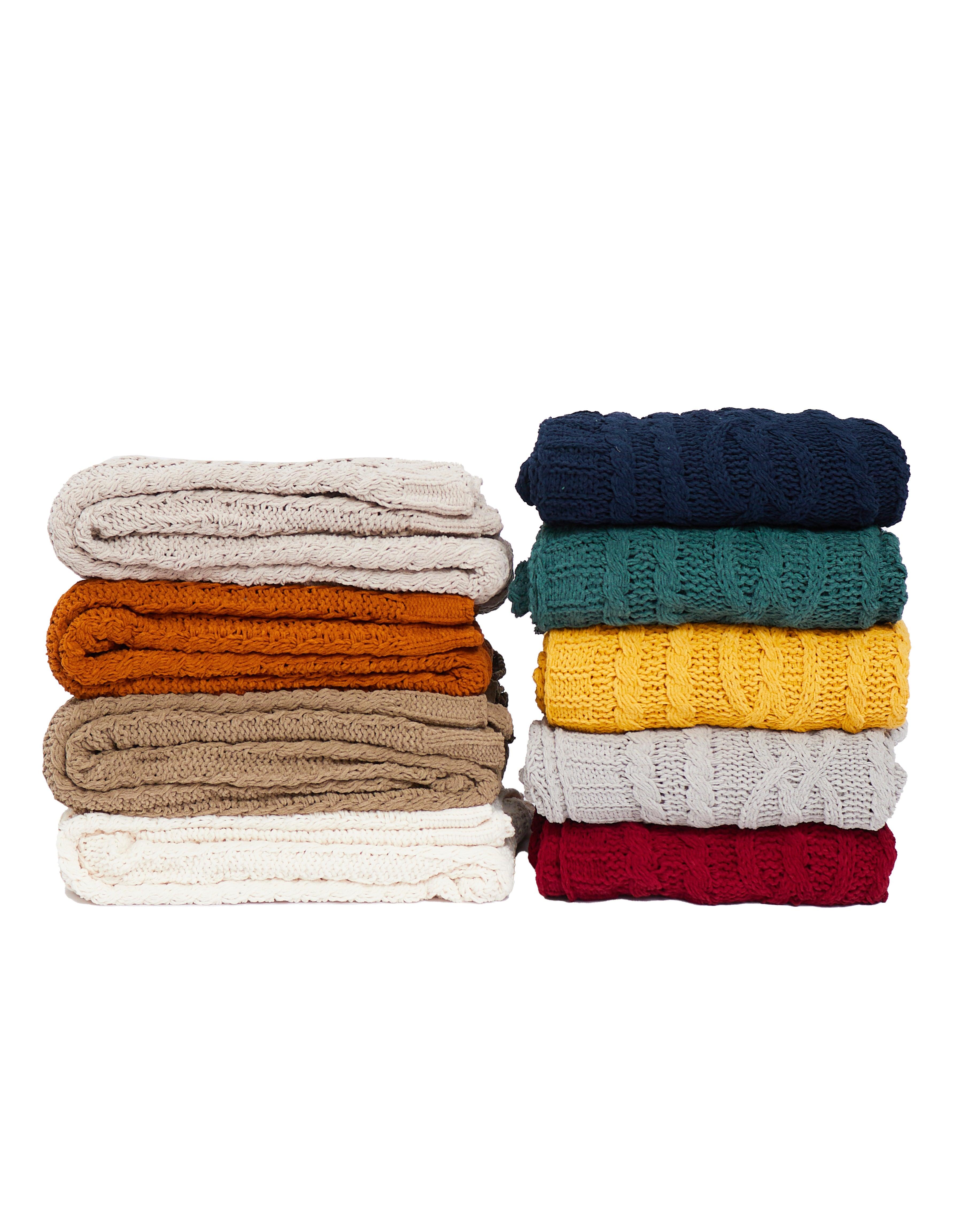 Stack of folded knitted Aurora Throw Blankets in vibrant colors including navy, teal, yellow, red, beige, orange, and white.