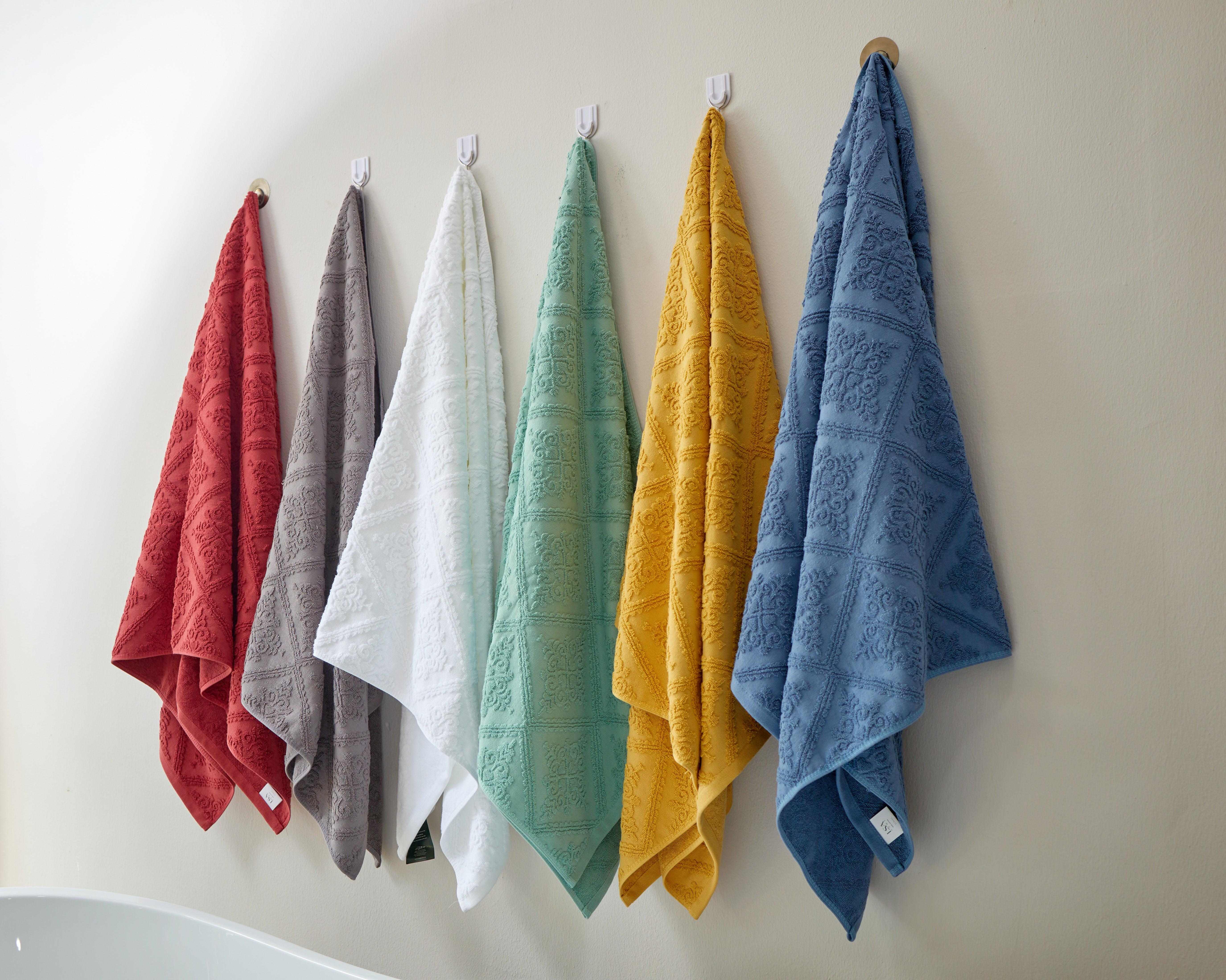 Karis Towel Collection in assorted colors with luxurious jacquard design hanging on a wall.