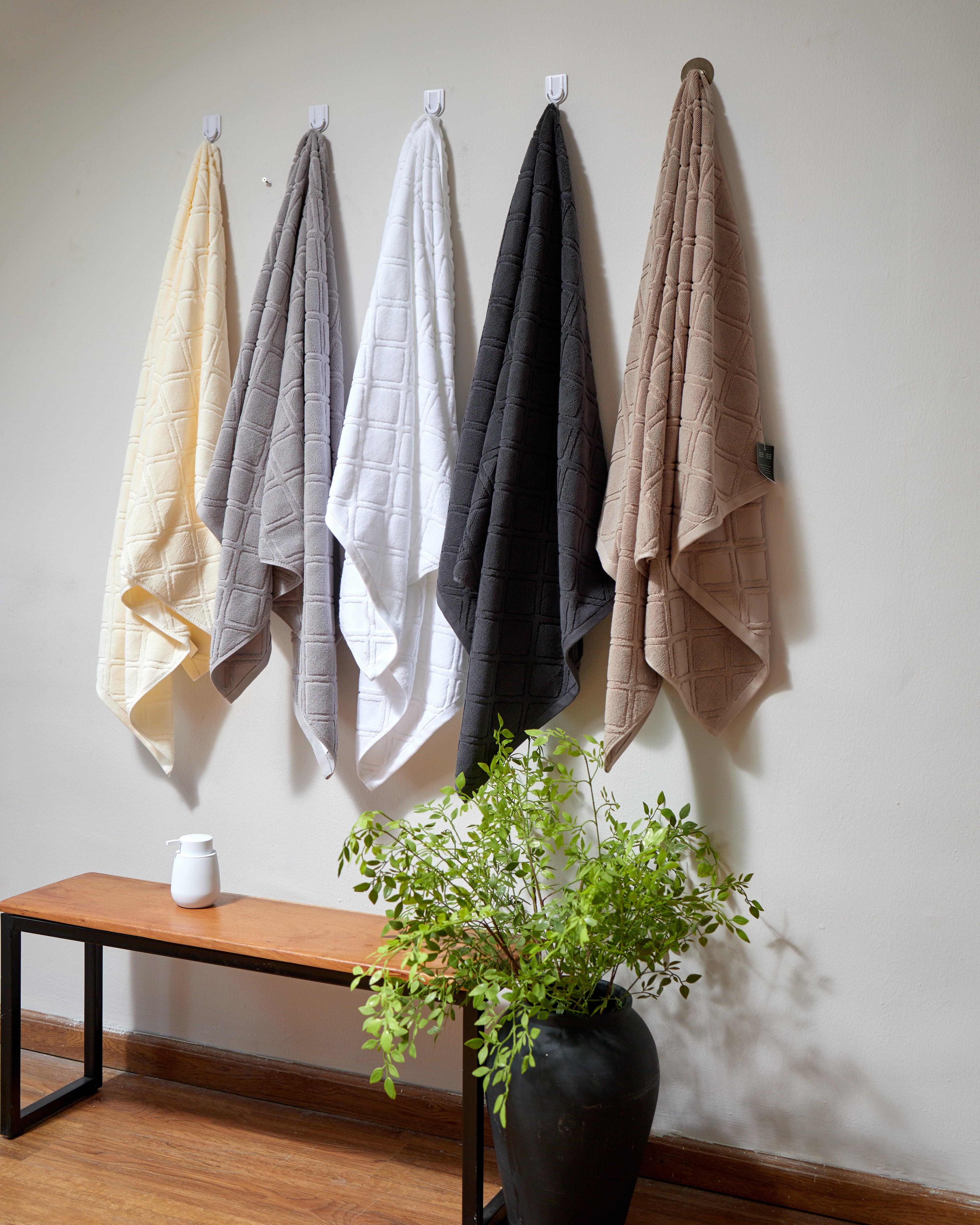 Gris Towel Collection hanging in various neutral colors on hooks above wooden bench with plant in black vase below