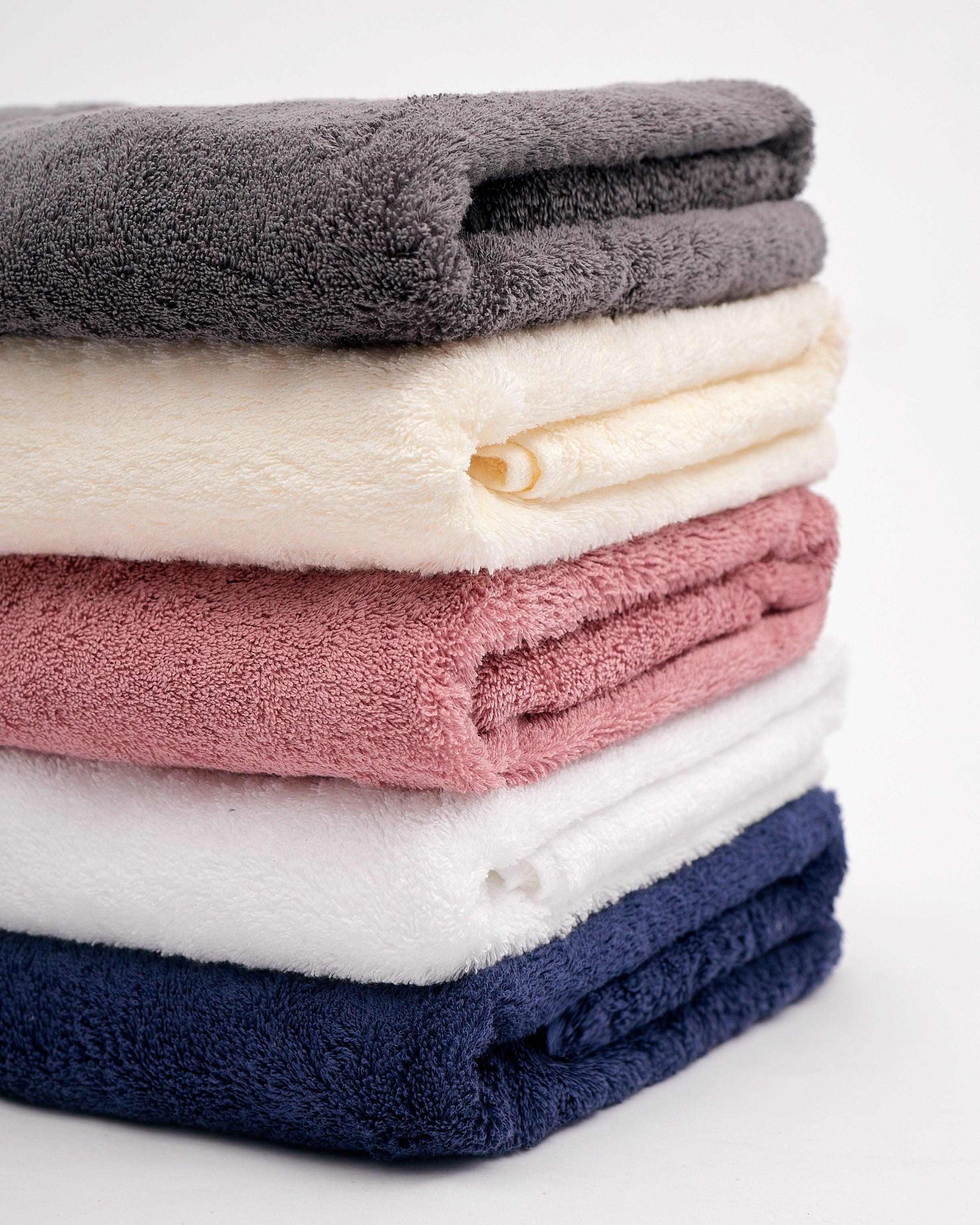 Stack of folded Deluxe Bath Sheet towels in various colors showing soft, absorbent 100% cotton material