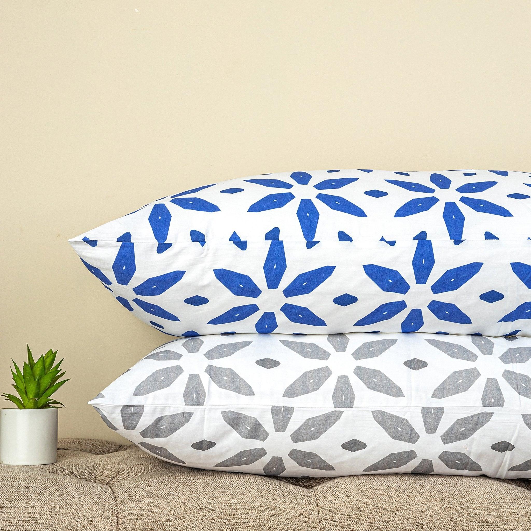 Two pillowcases with blue and grey crystal pattern designs stacked on a beige surface next to a small green potted plant