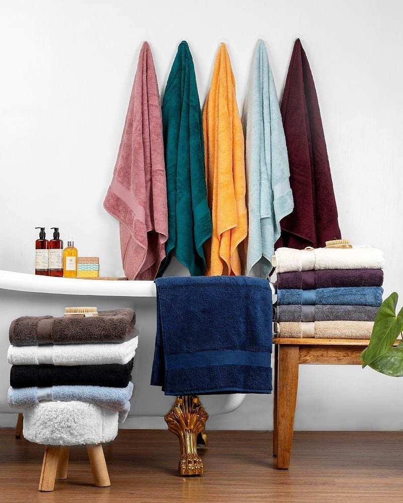 Assorted colorful deluxe bath towels made from plush Turkish cotton displayed hanging and folded near a bathtub.