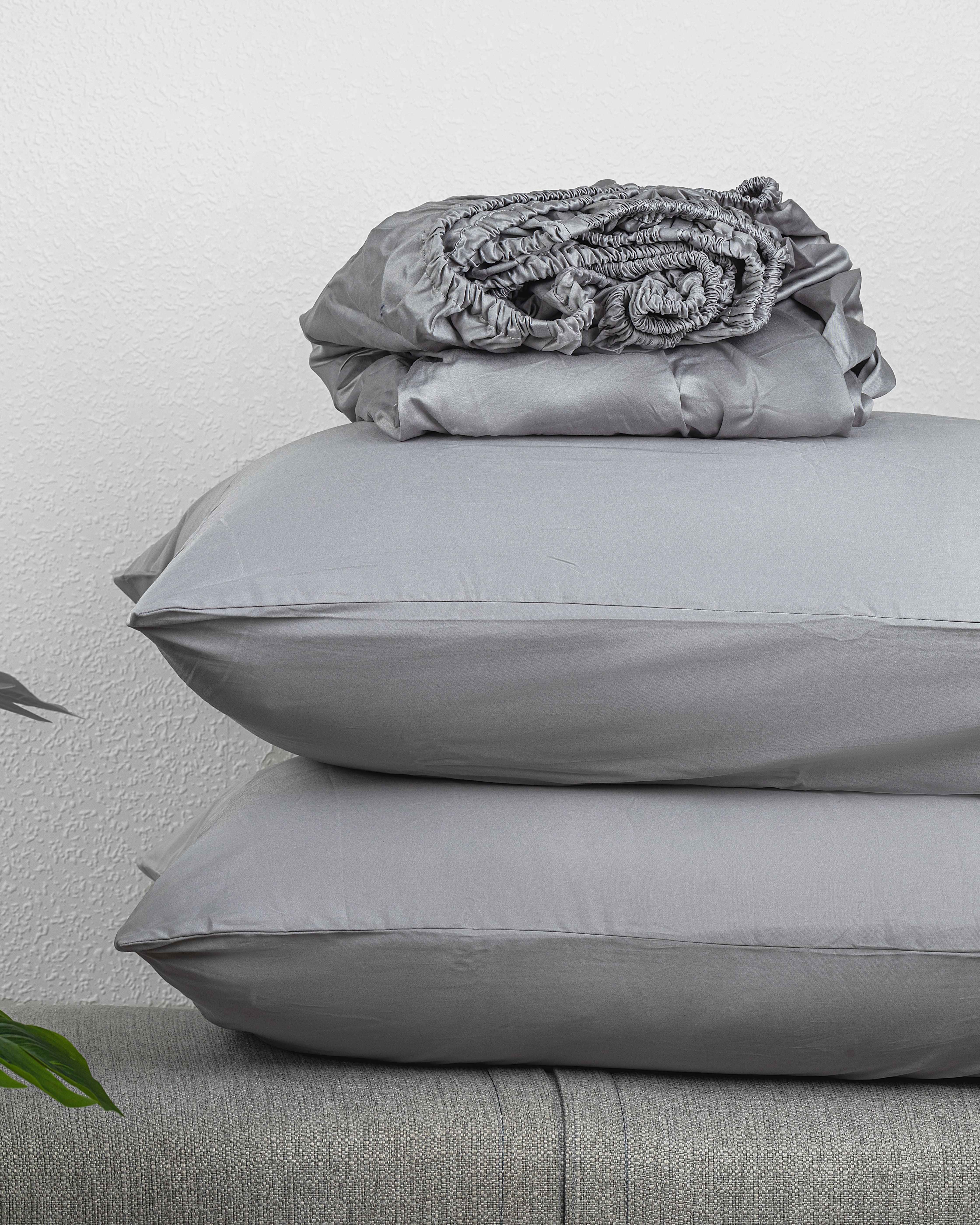 soft gray Luxe Kids Fitted Sheet set with pillowcases stacked on a gray surface against a white wall