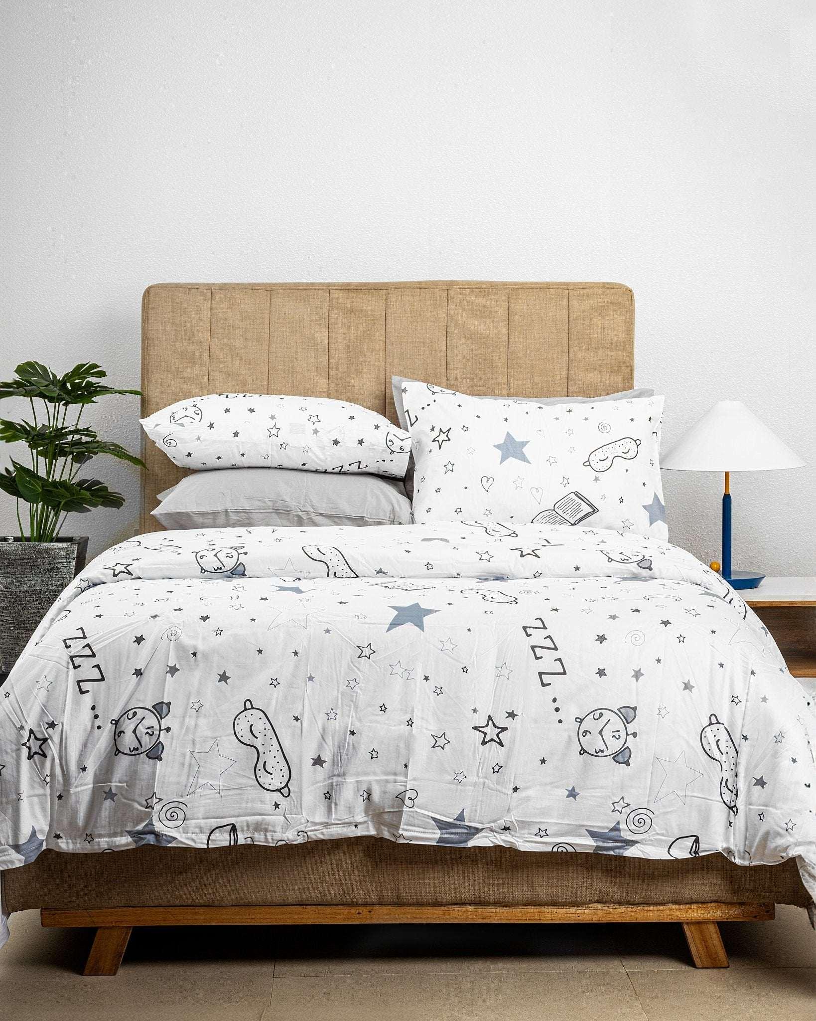 Snooze Kids Duvet Cover Set with stars, eye masks, and bedtime storybook prints on 100% cotton fabric with 1 duvet cover and 2 pillowcases on a bed